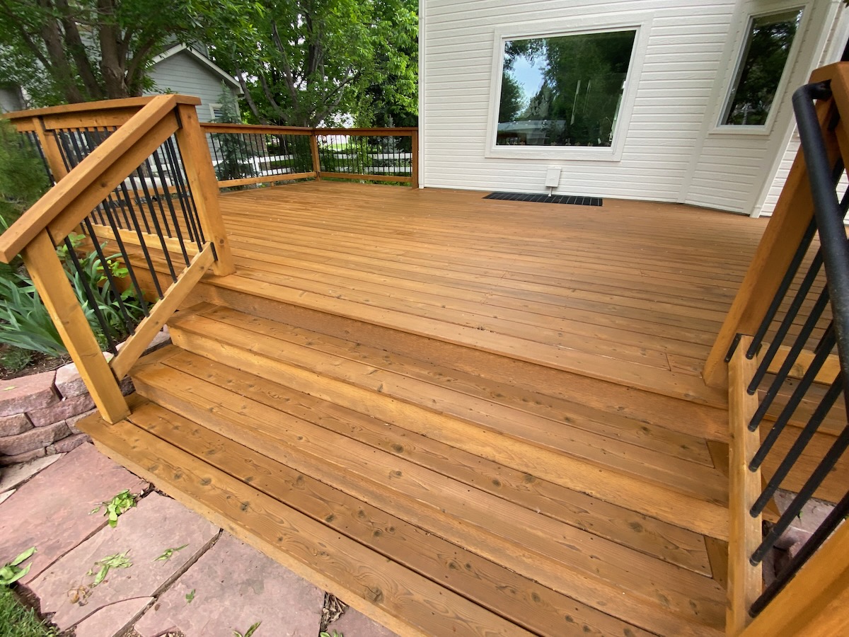 Freshly stained cedar deck with stairs and iron-baluster railing on a Wichita, Kansas home — professional deck staining protecting wood from Kansas weather